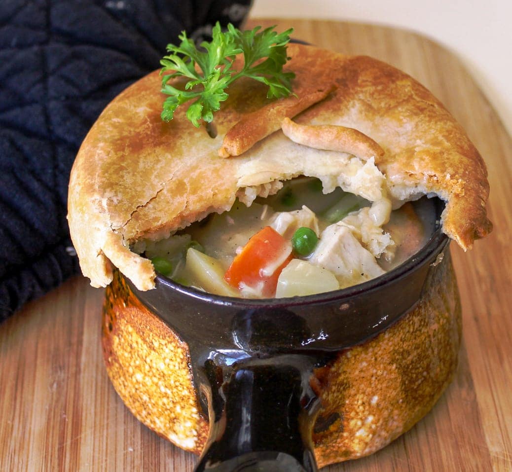 Individual Chicken Pot Pies with part of crust cut open peering inside sitting on cutting board