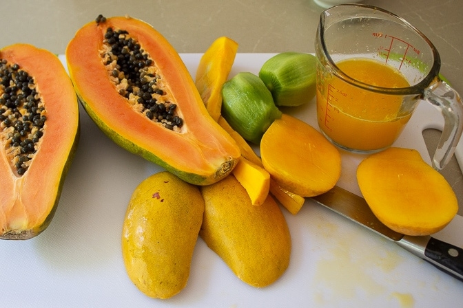 mango kiwi papaya cut open on cutting board with juice of oranges in measuring cup