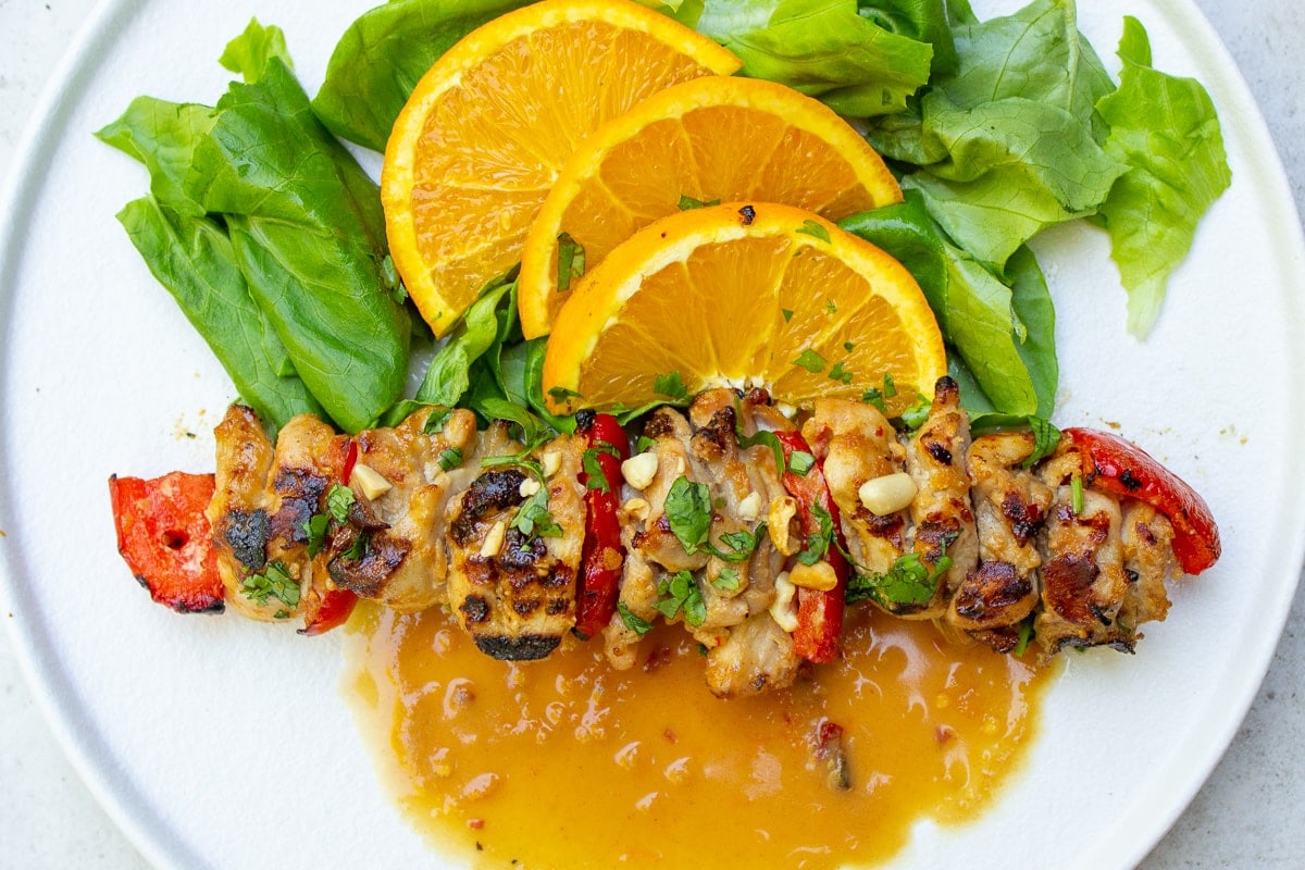 cooked chicken skewers on plate with oranges