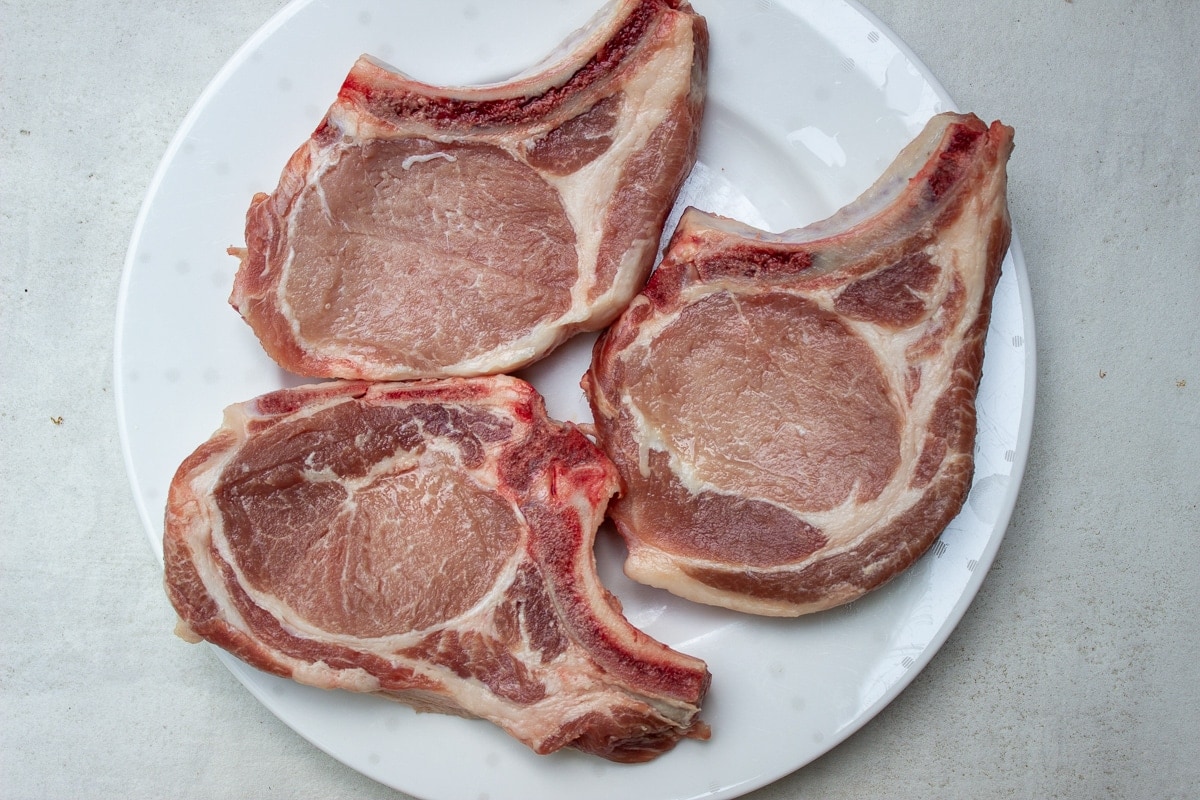 3 uncooked rib pork chops on plate