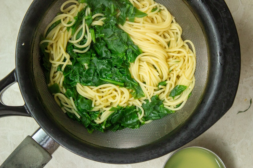 cooked spaghetti and spinach in strainer