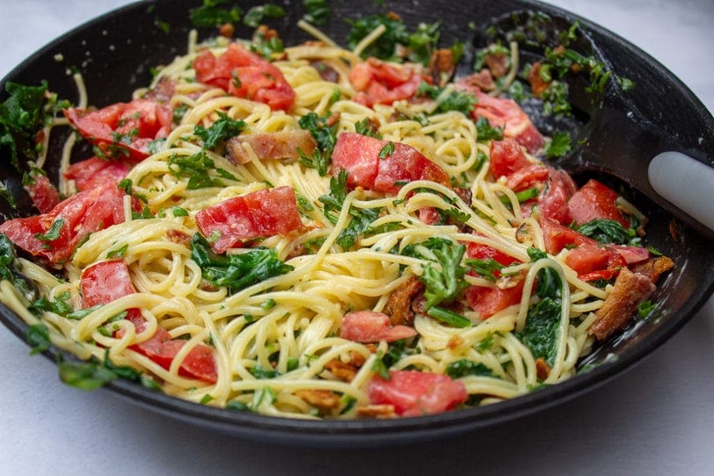 spaghetti carbonara with tomatoes and spinach in pan