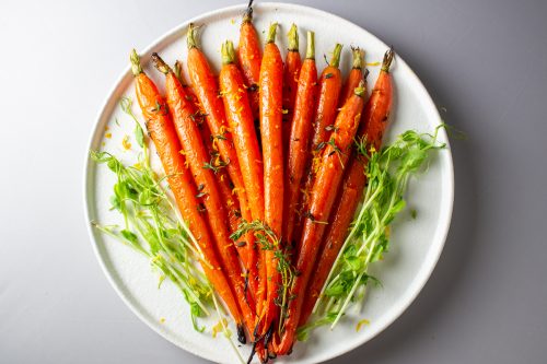 Roasted Honey-Thyme glazed Carrots on a plate garnished with orange zest and thyme