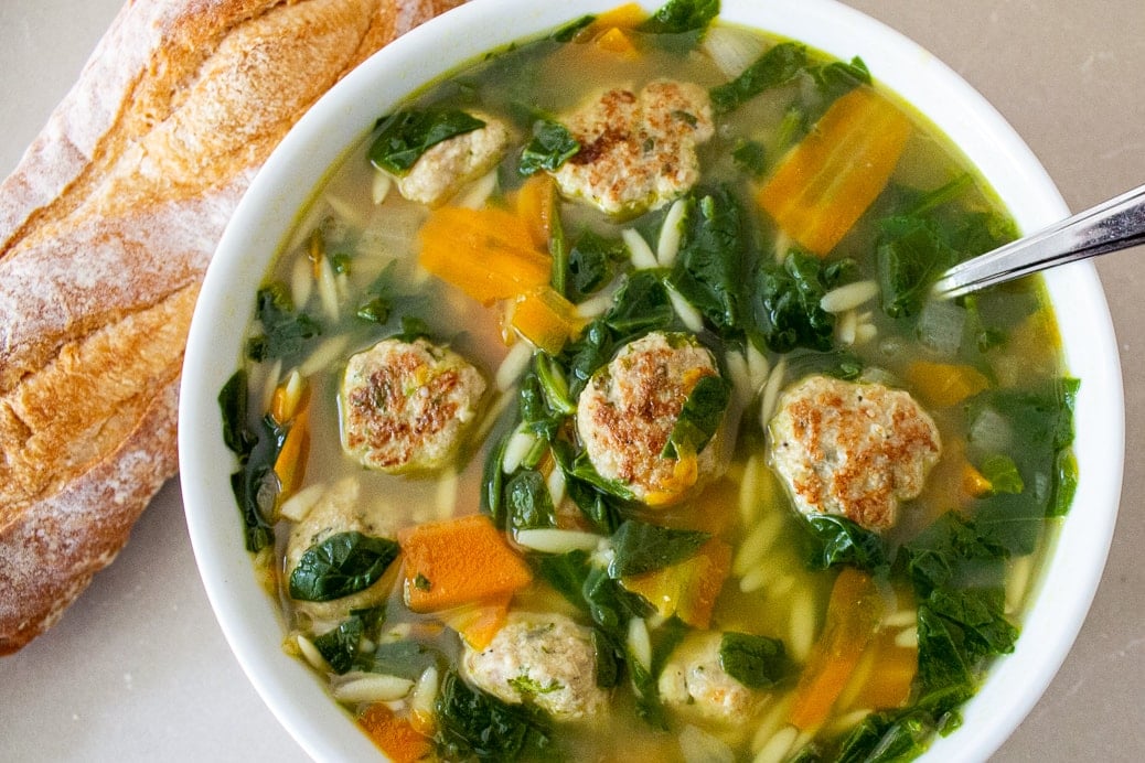 wedding soup in a bowl beside loaf of bread