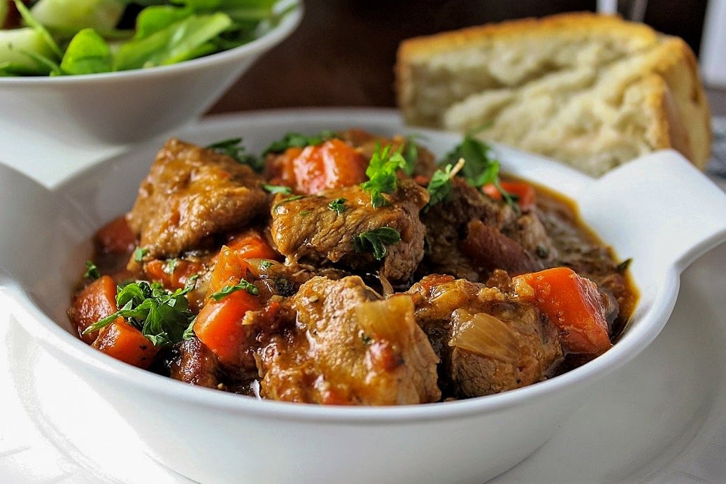 veal stew in a bowl with bread and salad on side