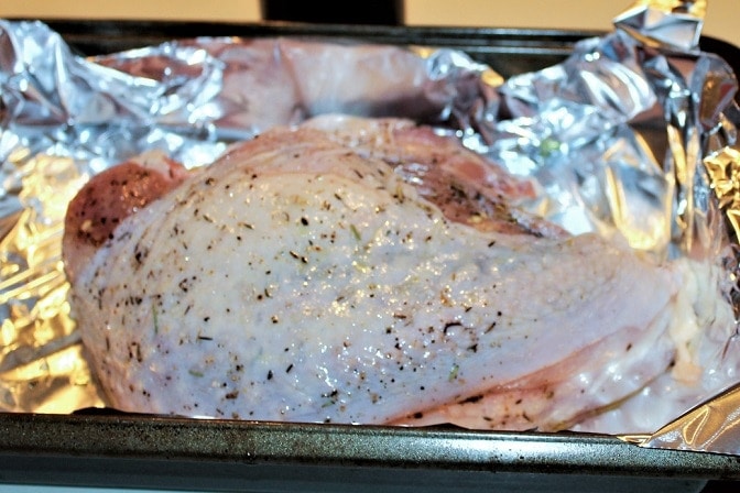 half turkey breast with seasoning in pan ready to roast