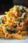 tomato spinach pasta lifted on fork over bowl
