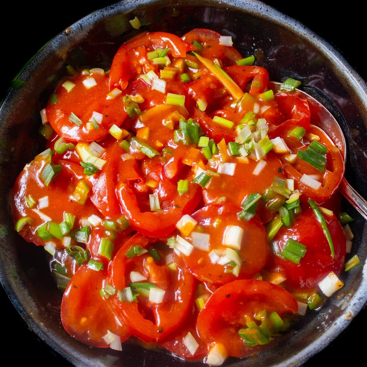 tomato onion salad in dressing in a black bowl