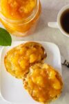 peach marmalade on english muffin on plate with jar of marmalade beside and coffee p1