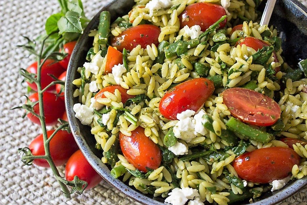 pesto and vegetable orzo in a bowl with vine tomatoes beside bowl