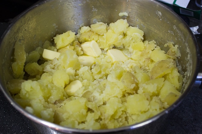 cooked potatoes in pot with butter and milk on top