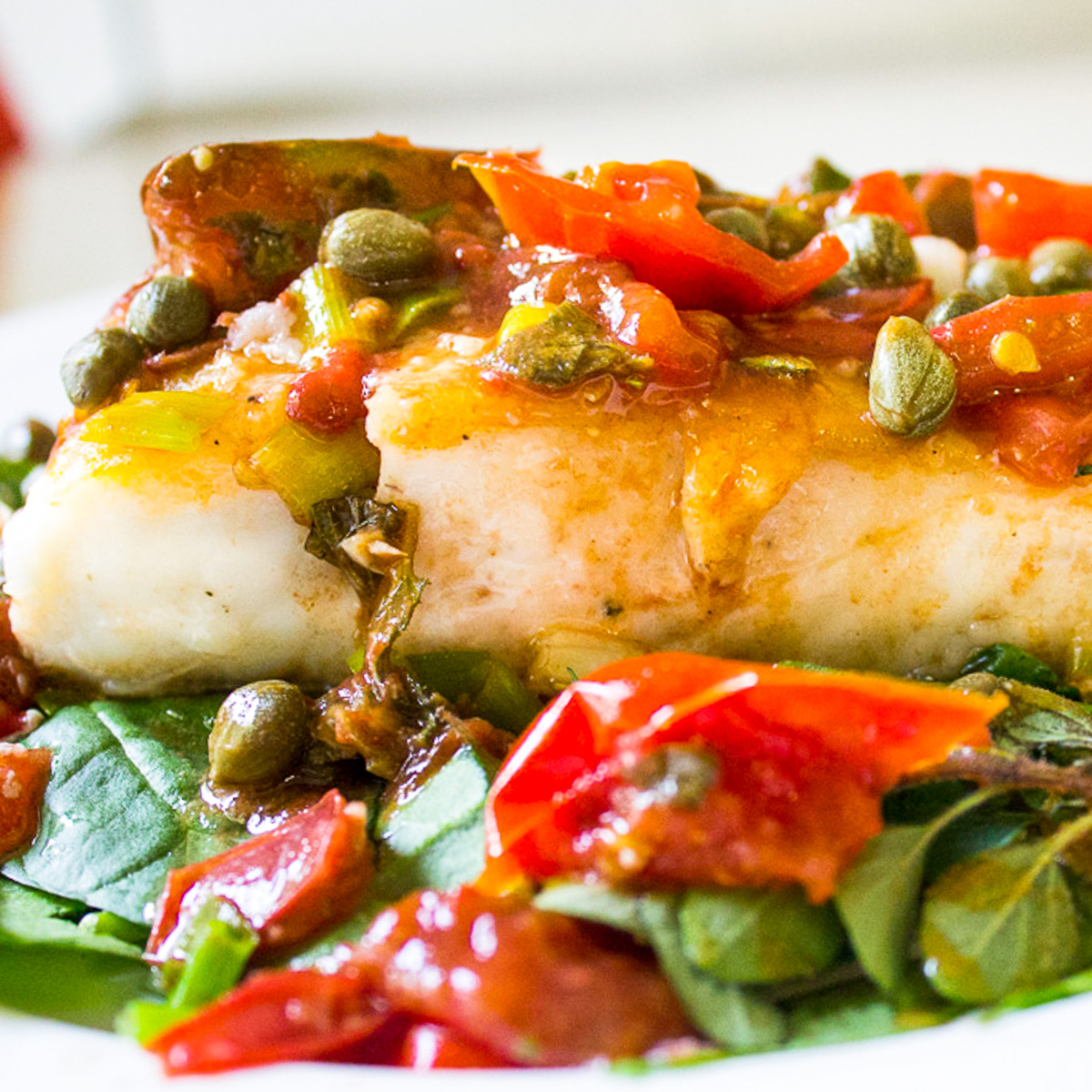 halibut with tomatoes and capers over spinach on plate