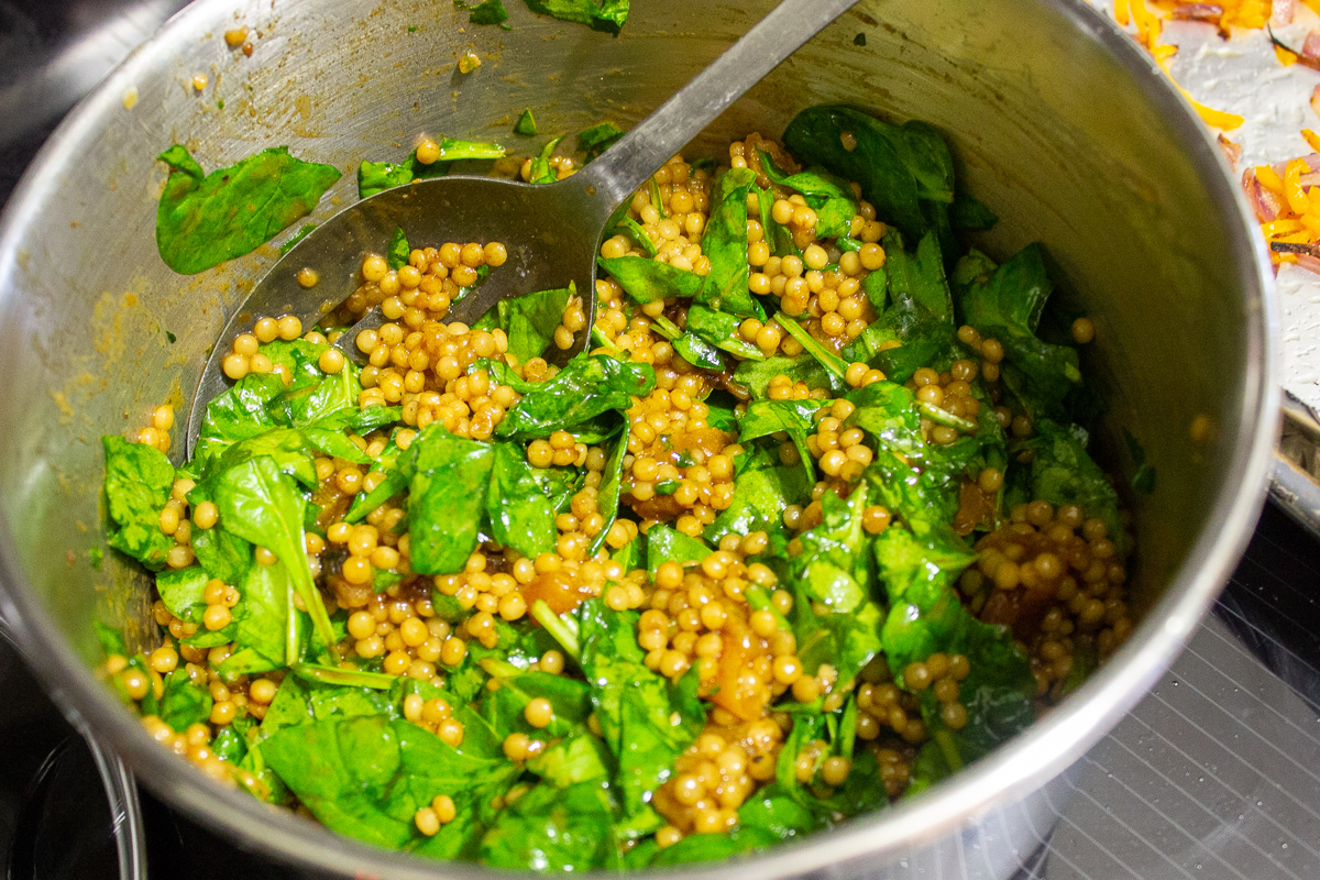 spinach added to cooked couscous in pot