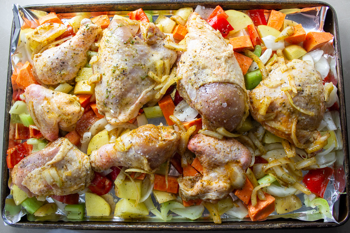 raw chicken pieces on vegetables on pan