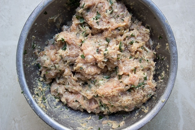 raw chicken burger mixture with seasonings and fillings in a mixing bowl