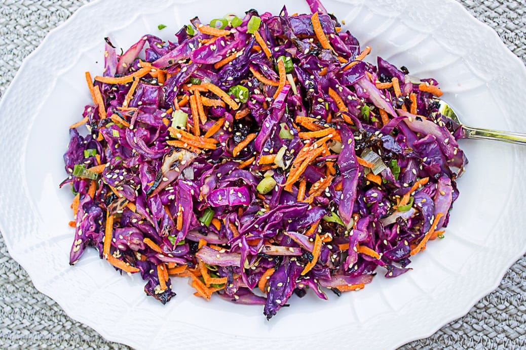 Grilled shredded cabbage with julienne carrots, green onion, sesame seeds and dressing on a platter.