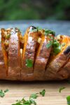 Grilled Hasselback Sweet Potato topped with maple pecan glaze on a cutting board p
