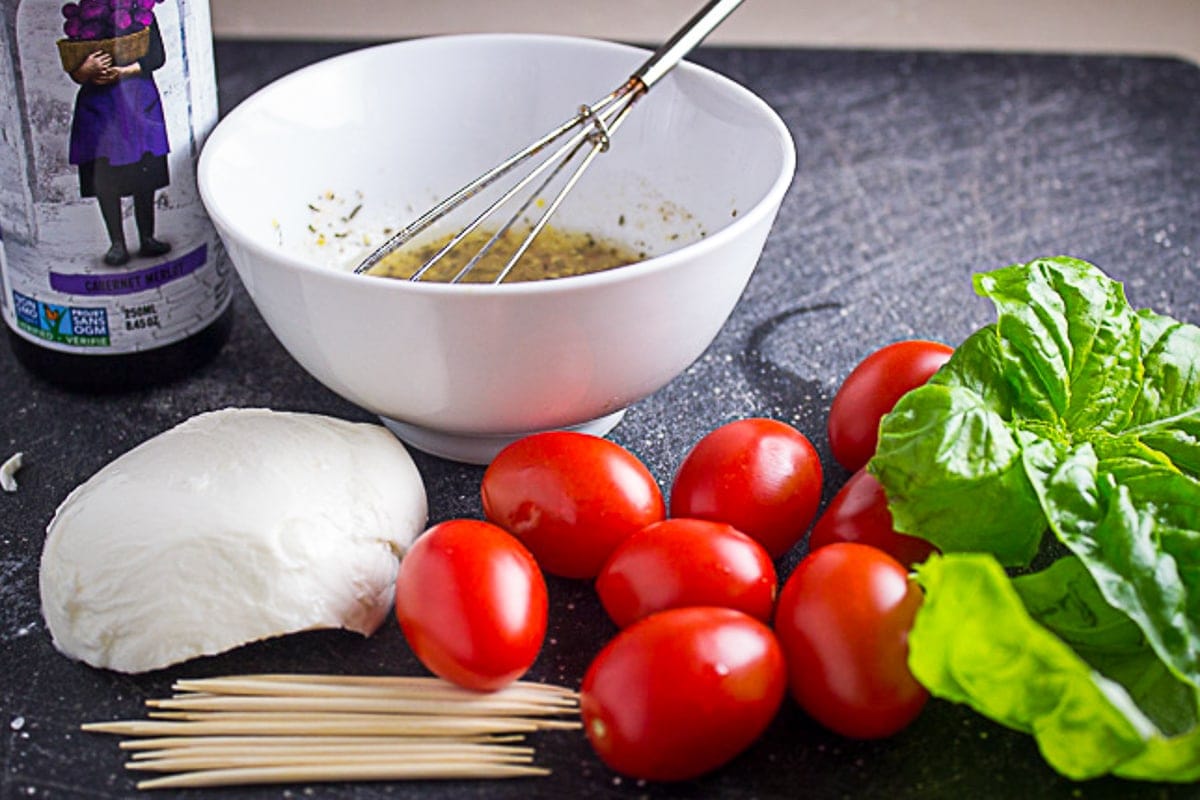 marinade in bowl, cheese, cherry tomatoes, toothpicks, basil leaves