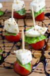 mini Caprese appetizers on toothpicks sitting on cutting board drizzled with balsamic reduction