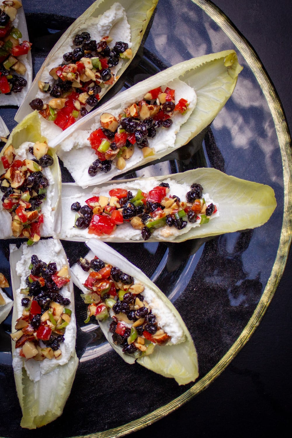 endive appetizers with ricotta, nuts, peppers and cranberries on black plate.