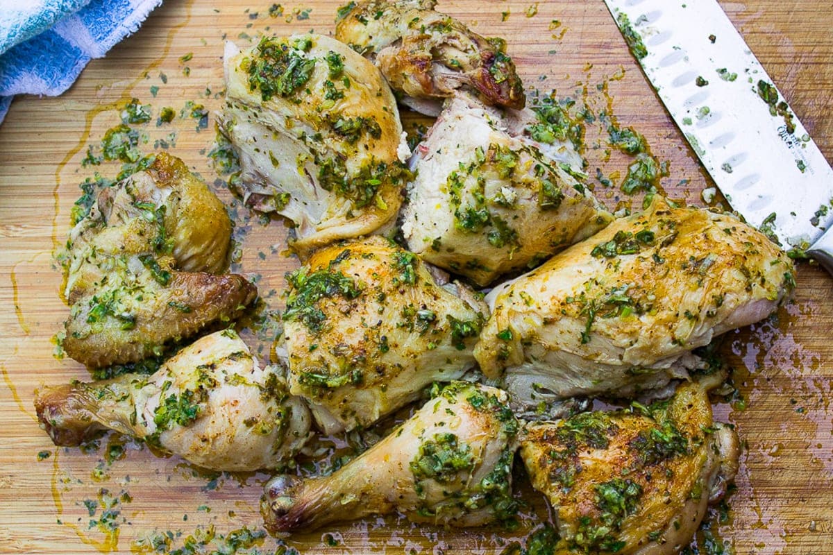 cut up chicken on cutting board mingled with herb sauce