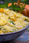 side view of bowl of pumpkin risotto on table beside pumpkin p2