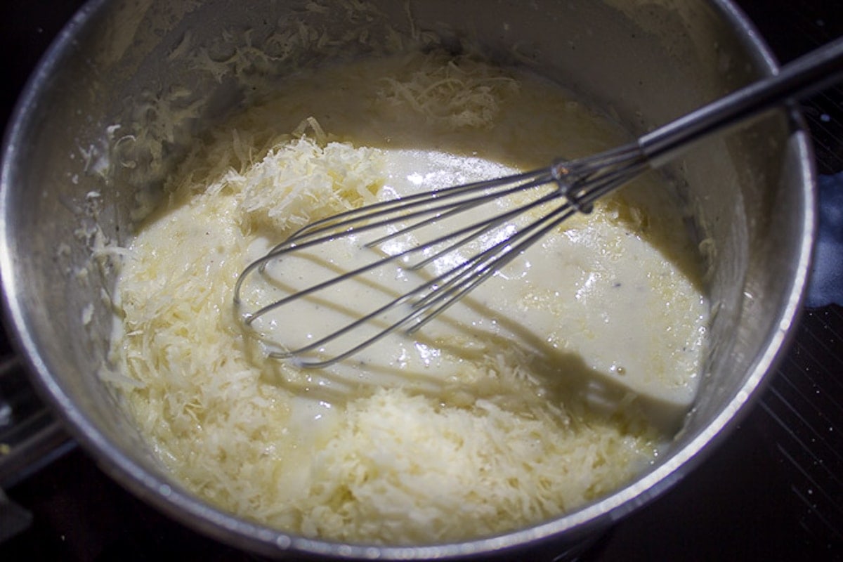 adding cheese to cream sauce in pot