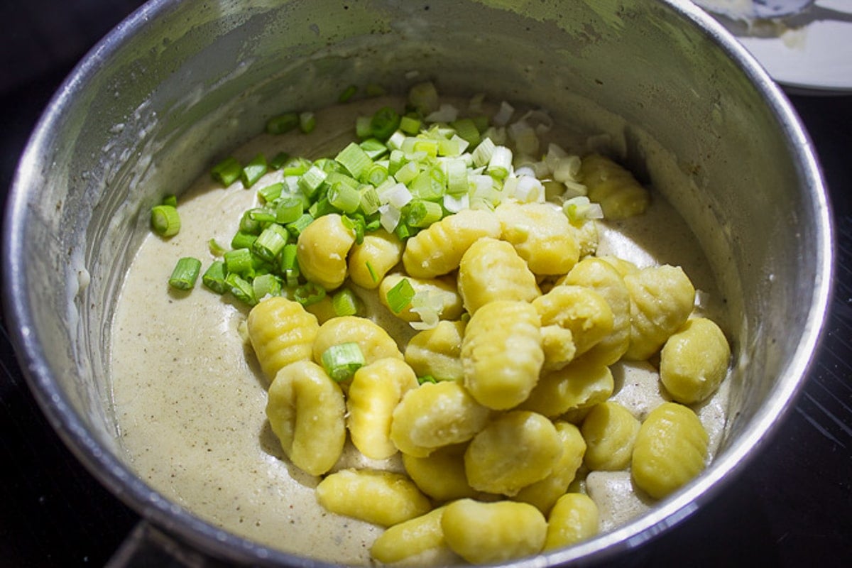 adding boiled gnocchi and green onions to cheese sauce in pot