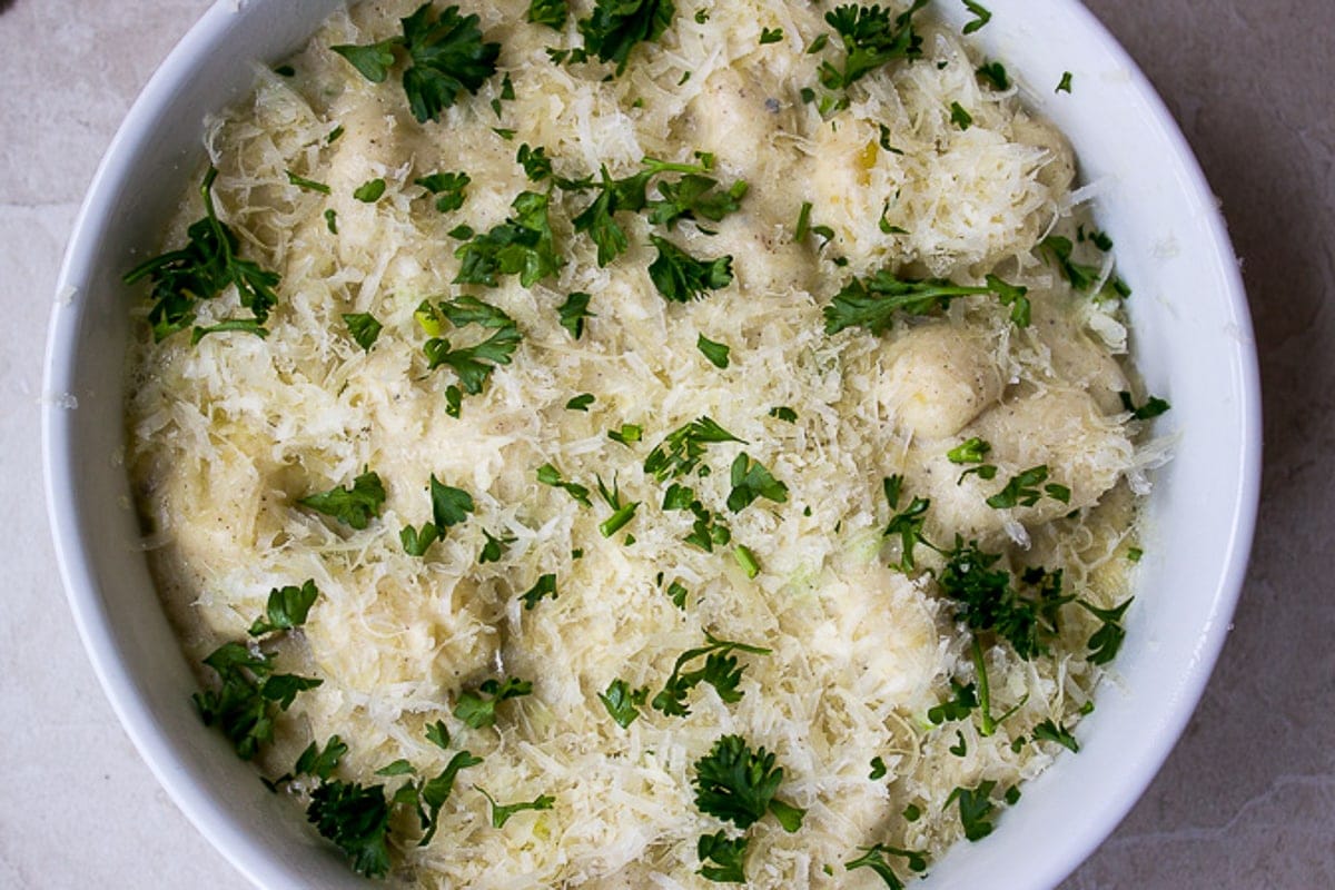 assembled gnocchi in cheese sauce with cheese on top ready to bake