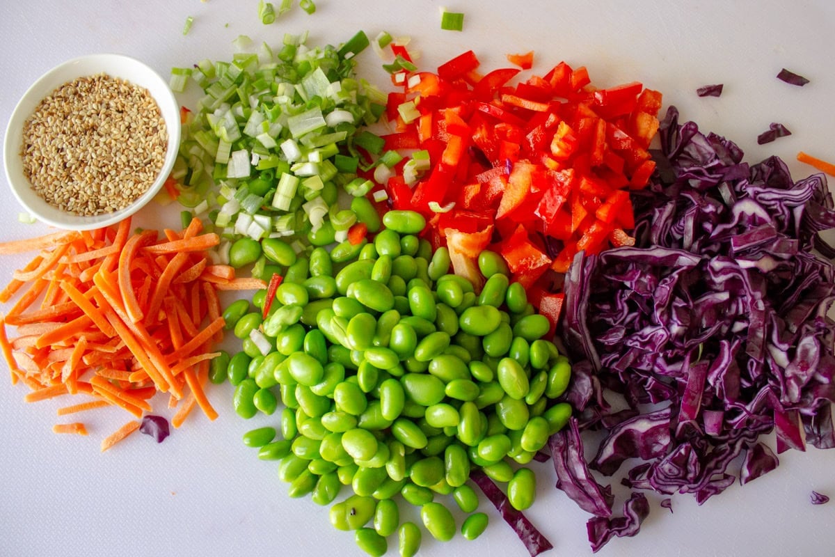 Chopped purple cabbage, carrots, red pepper, green onion and sesame seeds on cutting board.