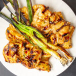 grilled chicken thighs on white plate with green onions
