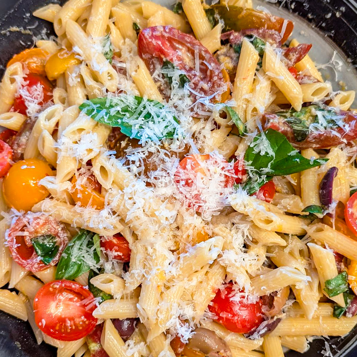 Serving bowl of tomato and basil pasta topped with parmesan cheese.