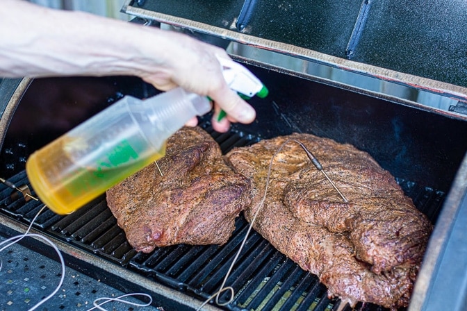 two briskets in smoker being sprayed with apple juice