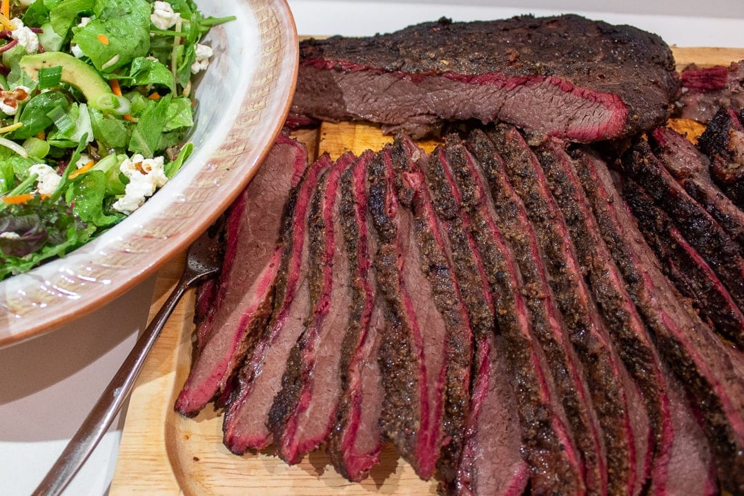 smoked brisket sliced on a cutting board served with salad