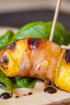 grilled peach wrapped in prosciutto on a toothpick laying on basil leaf p