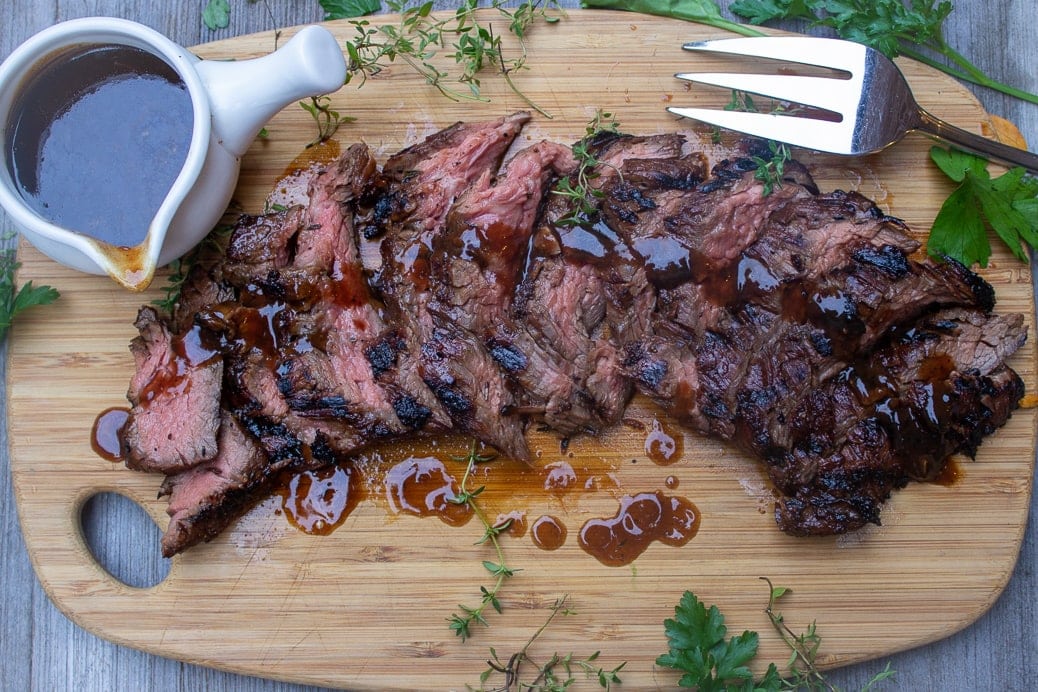 sliced marinated flank steak on cutting board with cup of sauce on side