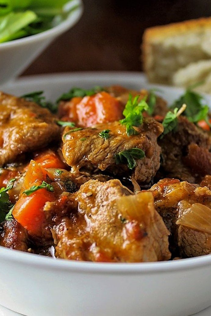 veal stew in a bowl with bread and salad on the side