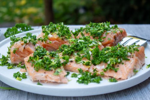Slow Roasted Salmon With Gremolata cut up on plate. garden in background