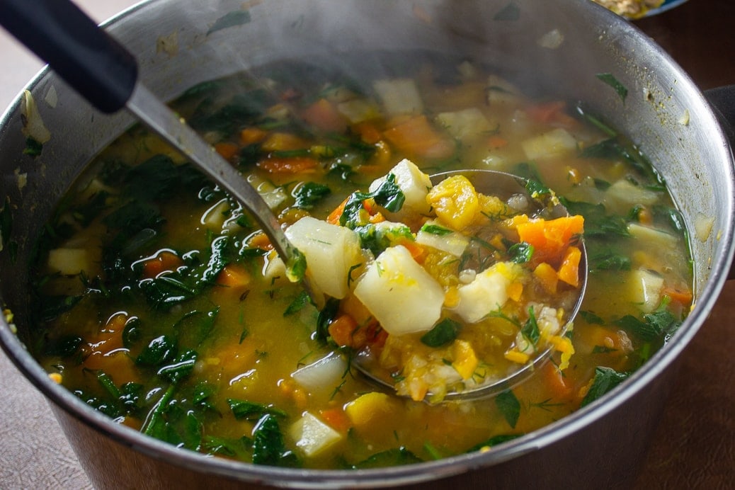finished root vegetable soup with spinach and dill added, showing veggies on a ladle over pot