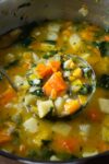 Root Vegetable Soup With Barley in pot with ladle scooping soup
