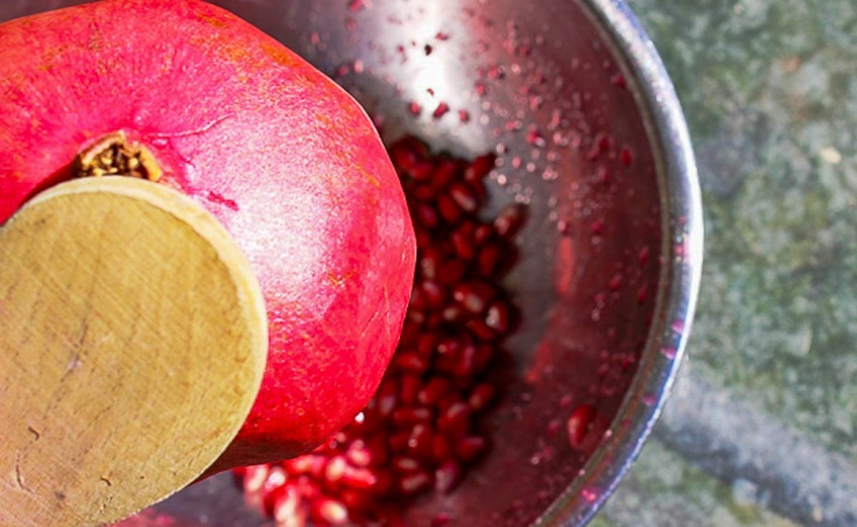 tapping pomegranate over bowl with spoon
