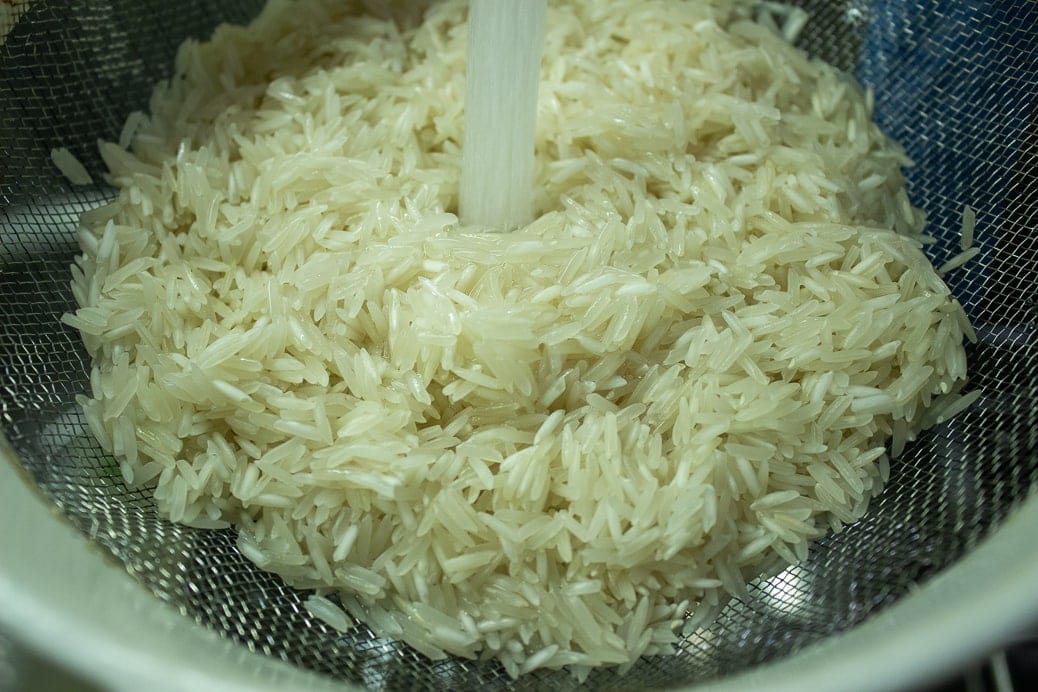 raw rice in strainer with water rinsing it