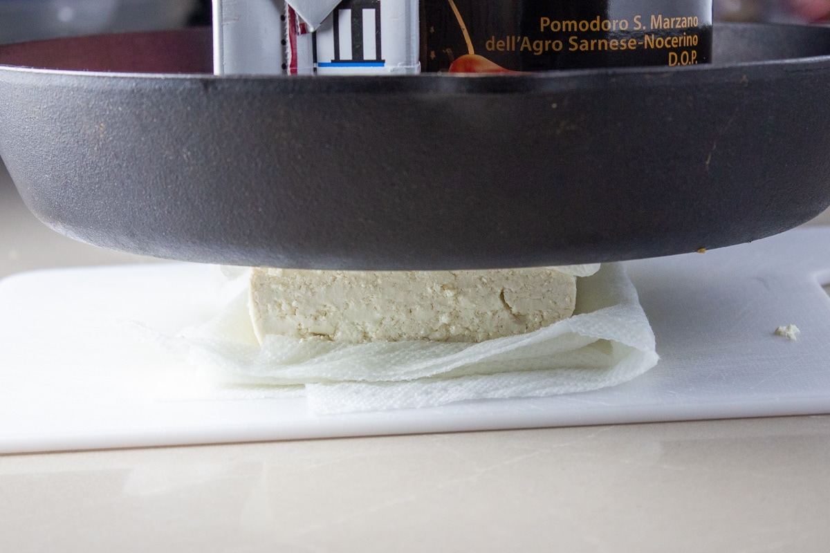 tofu squeezed under heavy pan on paper towel
