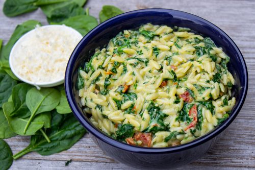 Parmesan Orzo with spinach in ceramic bowl on wood board with small bowl of Parmesan on side 1