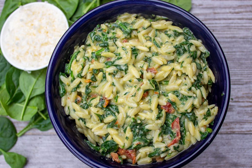 Parmesan Orzo with spinach in ceramic bowl on wood board with small bowl of Parmesan on side