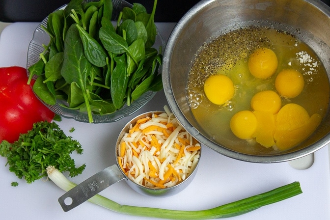 bowl with cracked open eggs, cheese, spinach, pepper, green onion