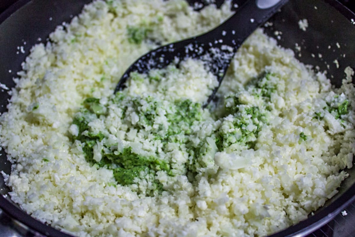 Cauliflower rice with added pesto in skillet with large spoon.