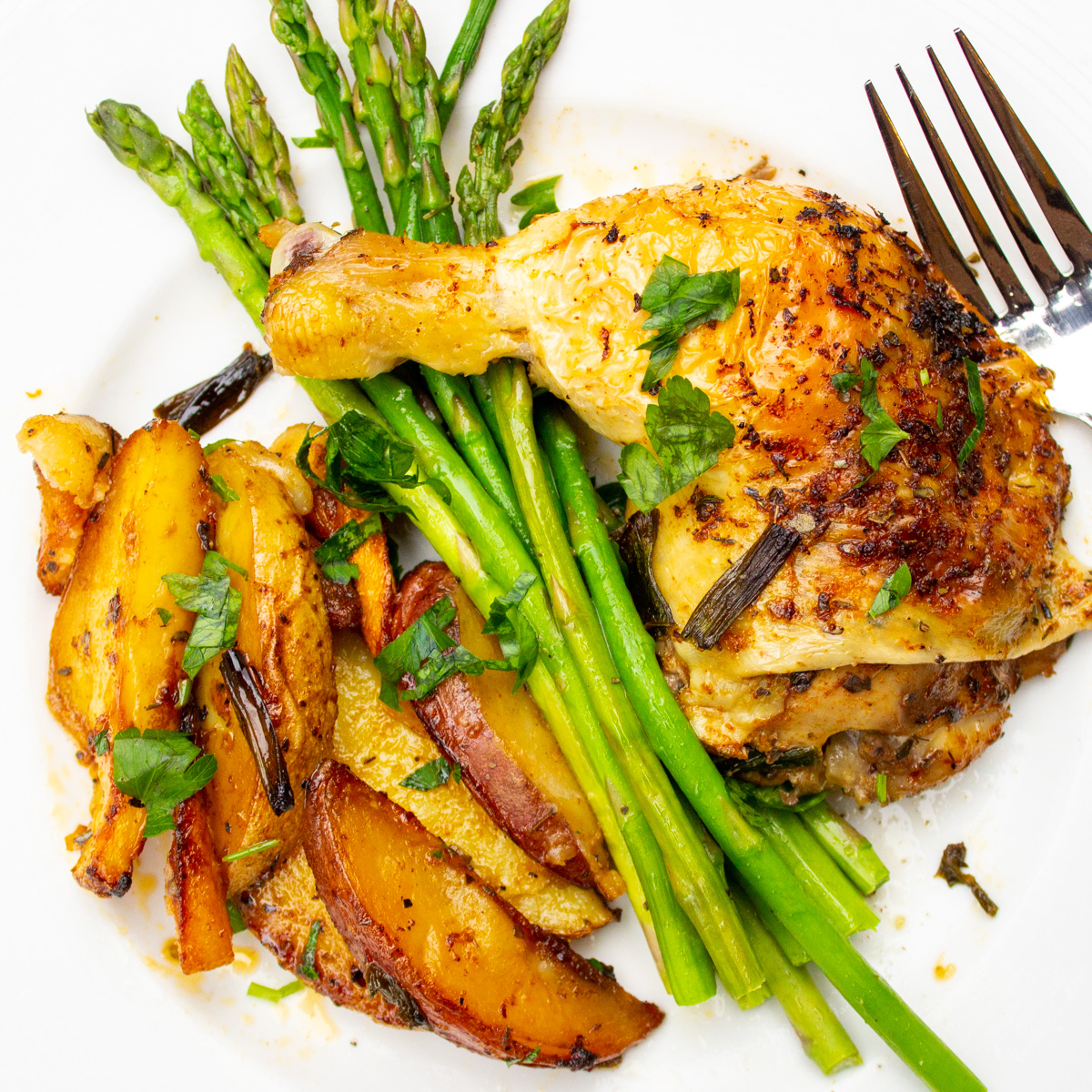 roasted chicken leg with roasted potatoes and asparagus on white plate