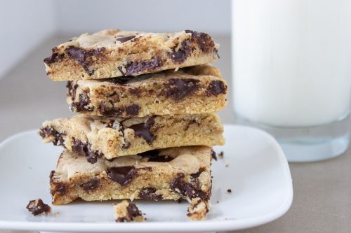 four chocolate chip cookie bars stacked on plate with milk beside it