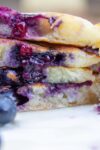 stack of lemon blueberry pancakes on plate cut in half showing inside with lots of blueberries p